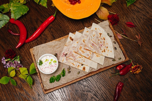 Deliciosos kutabs de pão plano gourmet com ervas e queijo em uma placa de madeira com molho