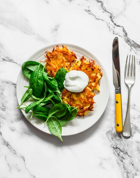 Deliciosos latkes de patatas de desayuno con crema agria y ensalada de espinacas en una vista superior de fondo claro