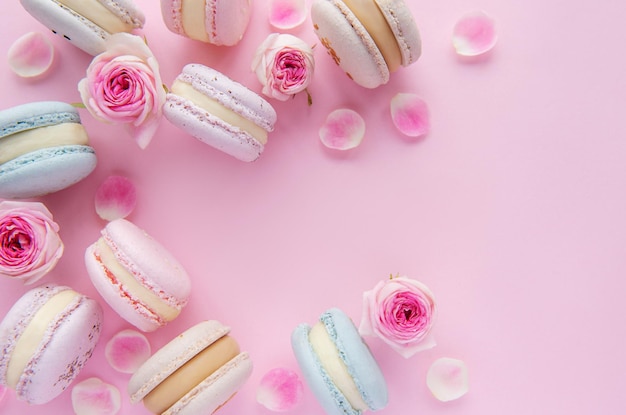 Deliciosos macarrones con hermosas rosas sobre un fondo rosa