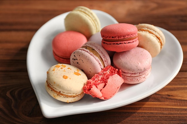 Deliciosos macarrones en placa con forma de corazón sobre fondo de madera