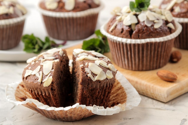 Deliciosos muffins de chocolate doce, com pétalas de amêndoa ao lado de hortelã e nozes de amêndoa em uma mesa leve de concreto. fechar-se