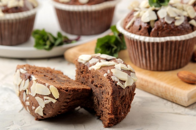 Deliciosos muffins de chocolate doce, com pétalas de amêndoa ao lado de hortelã e nozes de amêndoa em uma mesa leve de concreto. fechar-se