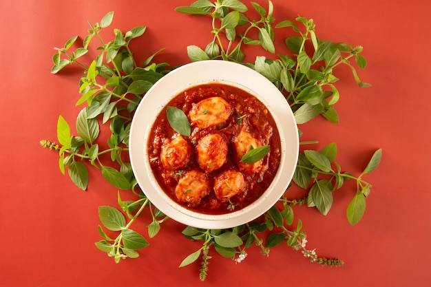 Deliciosos ñoquis con salsa roja y albahaca servidos en un tazón de cerámica hecho a mano con textura blanca en un fondo rojo y albahaca en la parte superior