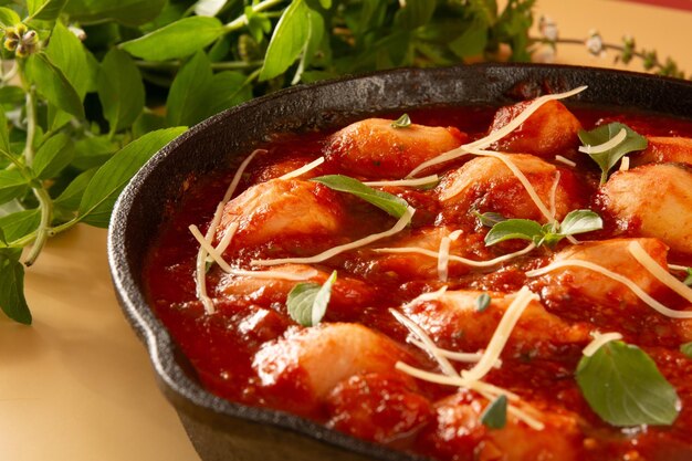 Deliciosos ñoquis con salsa de tomate rojo y albahaca servidos en una sartén negra con fondo beige al frente