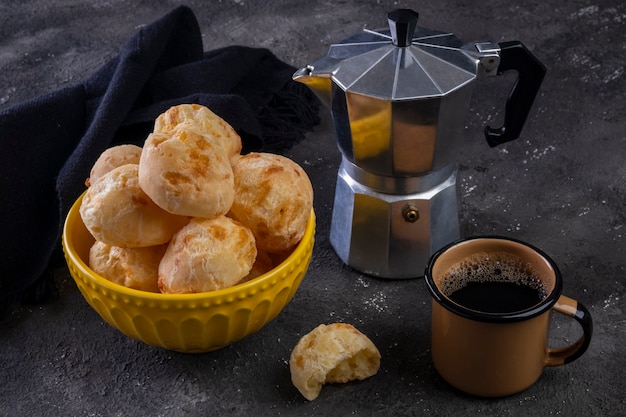 Deliciosos pães de queijo e uma caneca de café em fundo escuro.