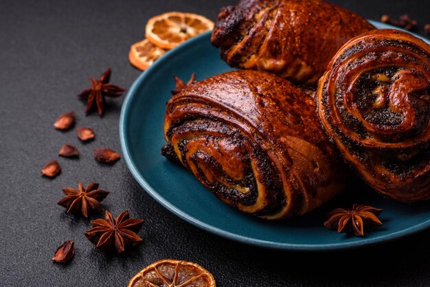 Deliciosos panes dulces y frescos horneados con semillas de amapola y canela en un plato de cerámica sobre un fondo de hormigón oscuro