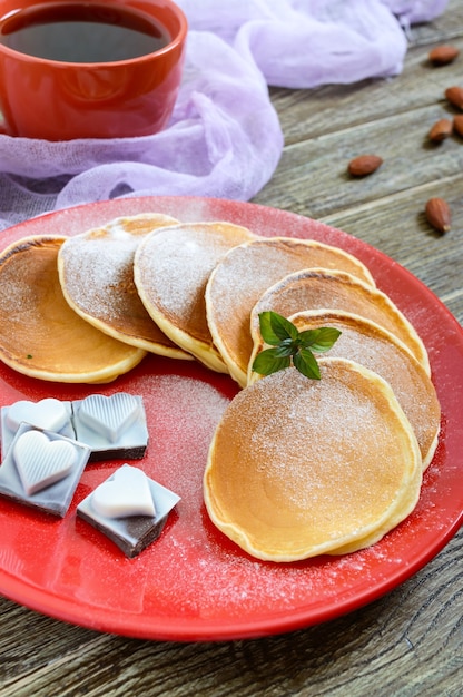 Deliciosos panqueques con azúcar en polvo en una placa roja sobre una mesa de madera