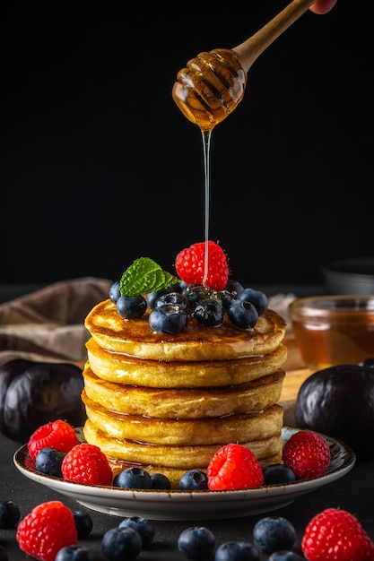 Deliciosos panqueques con bayas frescas y miel goteando