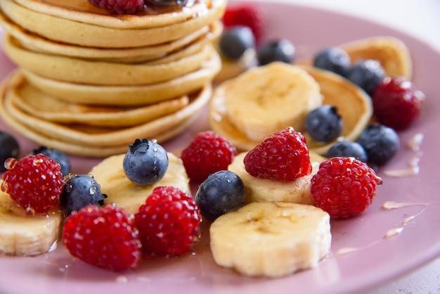 Deliciosos panqueques caseros con bayas frescas en un plato violeta Un sabroso y saludable desayuno de panqueques con frambuesas, arándanos y miel.