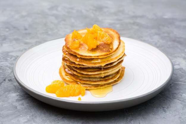 Deliciosos panqueques caseros con mandarinas y miel en un plato sobre la mesa