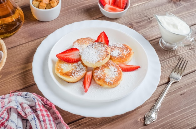 Deliciosos panqueques con fresas y azúcar en polvo en un plato blanco sobre un plato de madera oscura