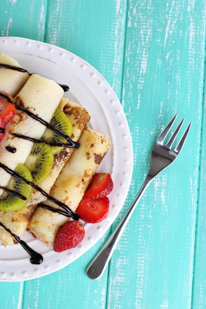 Deliciosos panqueques con fresas y chocolate en un plato en la mesa