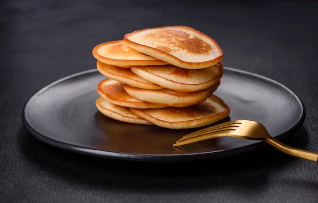 Deliciosos panqueques frescos en un plato negro sobre un fondo de hormigón oscuro