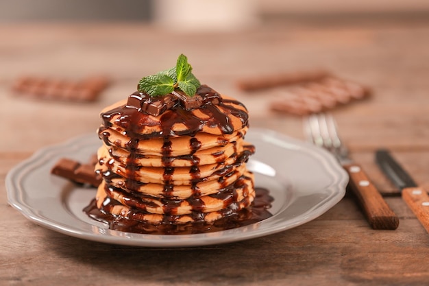 Deliciosos panqueques con jarabe de chocolate y menta sobre mesa de madera