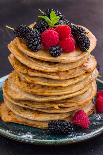 Deliciosos panqueques con moras, frambuesas y azúcar glas en un plato sobre la mesa negra