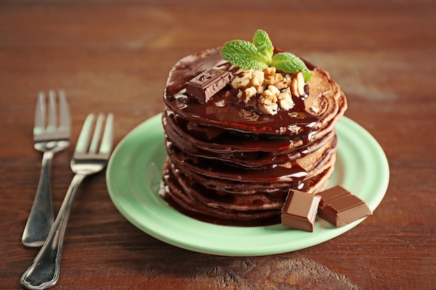 Deliciosos panqueques con nuez de chocolate y salsa dulce en un plato sobre fondo de madera