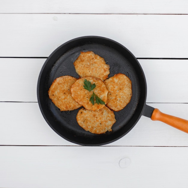 Deliciosos panqueques de patata en una sartén sobre una mesa de madera blanca