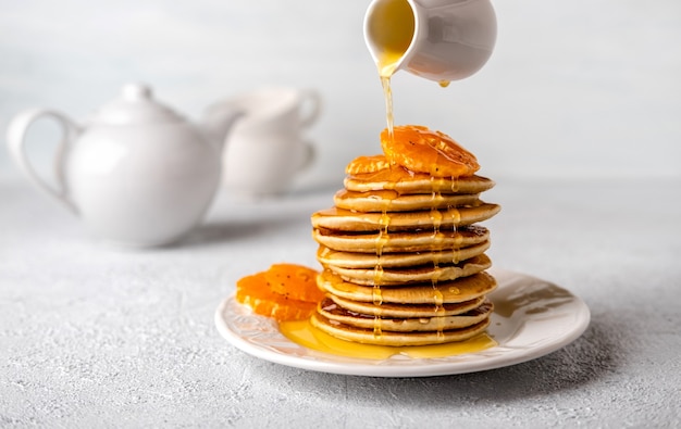 Deliciosos panqueques de primer plano con miel o jarabe de arce para el desayuno sobre un fondo claro. El almíbar se vierte sobre los panqueques.