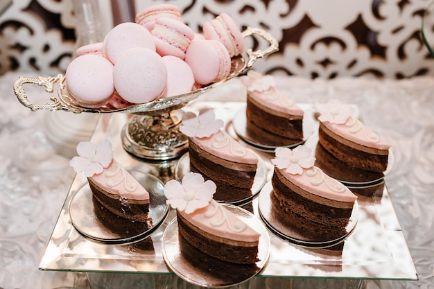 Deliciosos pasteles dulces de chocolate y vainilla y macarrones de color beige pastel rosa en un plato sobre una mesa dulce festiva de fondo con horneado