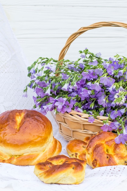 Foto deliciosos pasteles (pan y bollos con pasas) y lino bouquet en cesta de mimbre