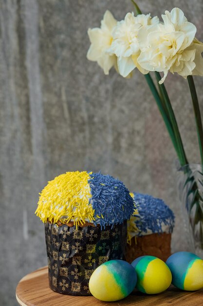 Deliciosos pasteles de Pascua en los colores de la bandera de Ucrania huevos de Pascua de color azul amarillo sobre una mesa de madera con flores en el lugar de fondo para el enfoque selectivo del texto