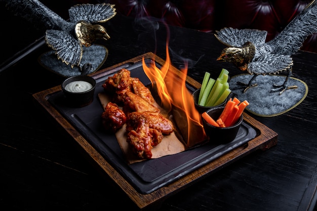 Deliciosos pedaços de asas de frango grelhados com chamas de fogo. No fundo preto do restaurante. Churrasco e grelhados. Prato de restaurante