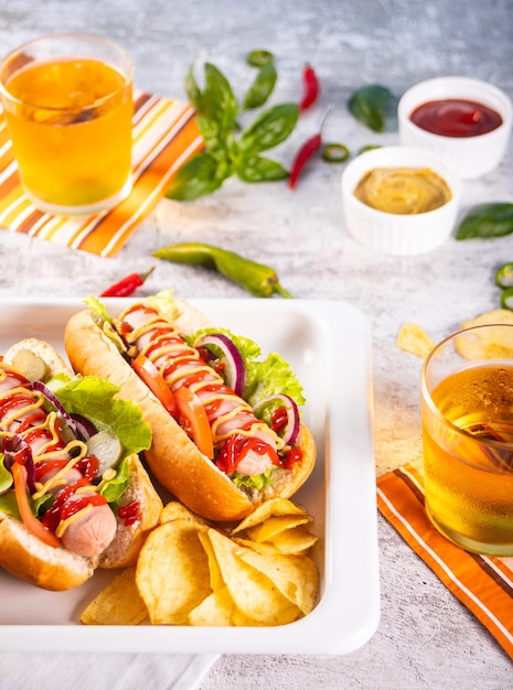 Deliciosos perritos calientes caseros con salsas, patatas fritas y vasos de cerveza en la mesa de madera Vista superior Espacio de copia