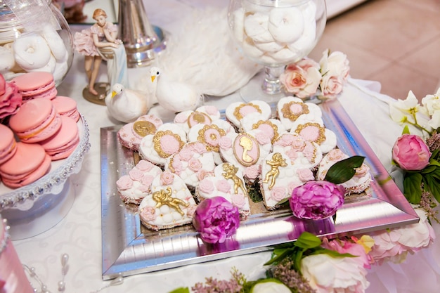 Deliciosos postres en la barra de chocolate de la boda en el área del buffet: galletas cubiertas con glaseado, decoradas con ángeles, camafeos, capullos de rosa de azúcar y tinte dorado.