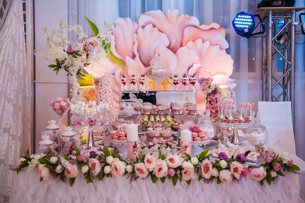 Deliciosos postres en el candy bar de bodas en el área de buffet velas decoradas capullos de rosa cintas macarons fresas en chocolate blanco