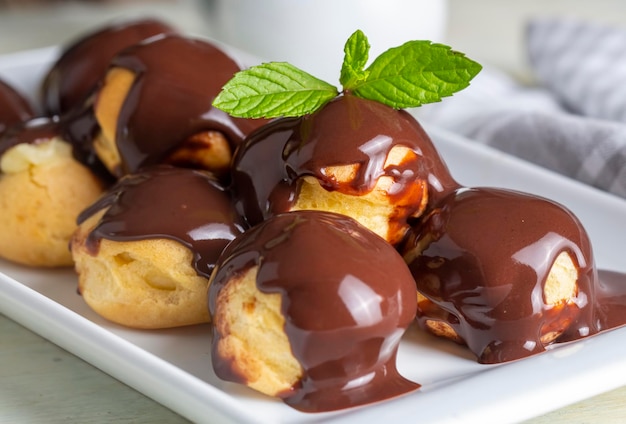 Deliciosos profiteroles com chocolate e placa branca. Imagem de foco seletivo em fundo claro.