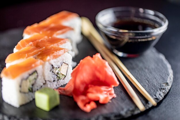 Deliciosos rollos de arroz de sushi en plato de piedra negra con salsa de soja y palillos