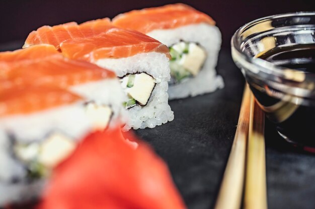 Deliciosos rollos de arroz de sushi en plato de piedra negra con salsa de soja y palillos