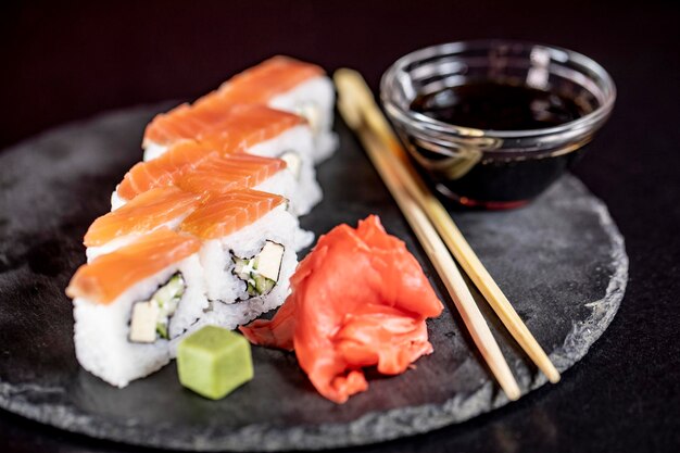 Deliciosos rollos de arroz de sushi en plato de piedra negra con salsa de soja y palillos