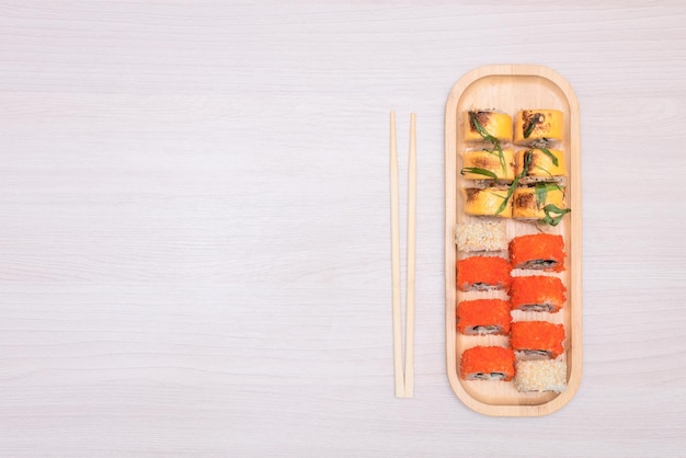 Deliciosos rollos japoneses con queso de salmón, aguacate y pepino en un plato de madera con palitos de madera con enfoque selectivo Concepto de comida asiática Alimentación saludable