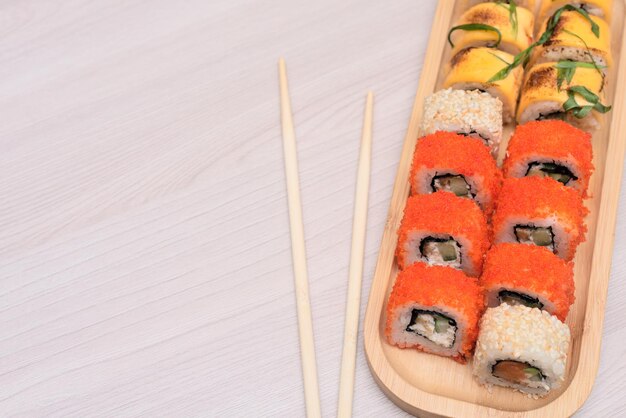 Deliciosos rollos japoneses con queso de salmón, aguacate y pepino en un plato de madera con palitos de madera con enfoque selectivo Concepto de comida asiática Alimentación saludable