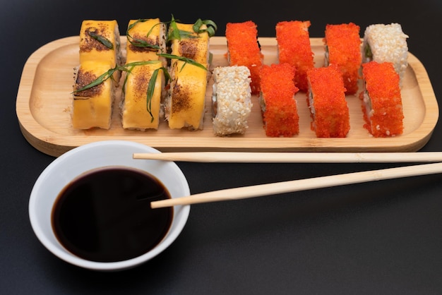 Deliciosos rollos japoneses con queso de salmón, aguacate y pepino en un plato de madera con palitos de madera y salsa de soja con enfoque selectivo en el fondo negro Concepto de comida asiática Alimentación saludable
