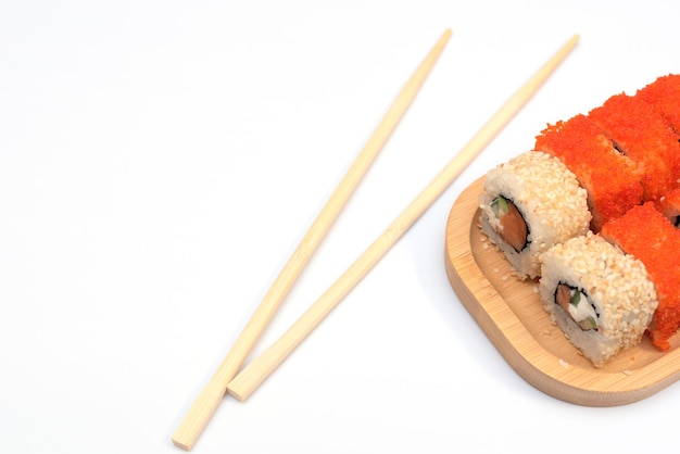 Deliciosos rollos japoneses con salmón aguacate pepino queso en placa de madera con palitos de madera con enfoque selectivo sobre fondo blanco Concepto de comida asiática Alimentación saludable