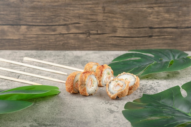 Deliciosos rollos de sushi caliente y palillos en la superficie de piedra.