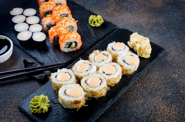 Deliciosos rollos de sushi y Maki en placa de piedra con salsas, palillos, jengibre y wasabi