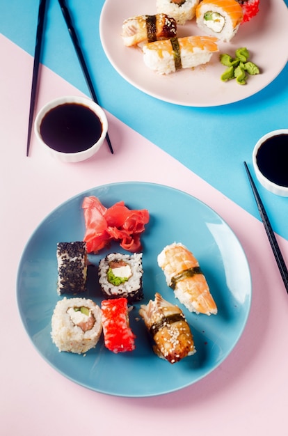 deliciosos rollos de sushi en placa azul con salsas, palillos, jengibre y wasabi en el fondo.