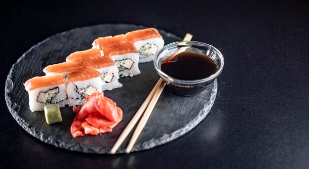 Deliciosos rolos de arroz de sushi na placa de pedra preta com molho de soja e pauzinhos