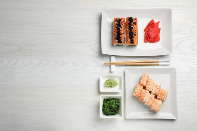 Deliciosos rolos de sushi servidos em mesa de madeira branca plana Espaço para texto
