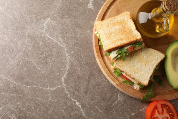 Deliciosos sándwiches, aceite, aguacate y tomate sobre fondo gris, espacio para texto