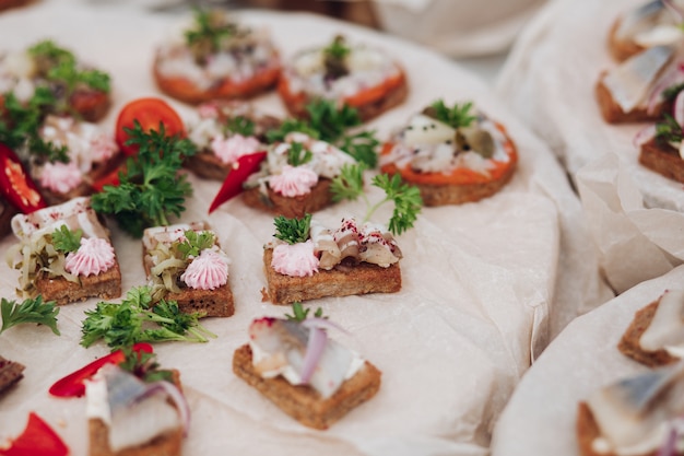 Deliciosos sándwiches con arenque y cebolla. Primer plano de sabrosos sándwiches crujientes o canapés con queso crema, cebolla y arenque en la parte superior. Perejil y guindilla en el plato.