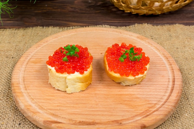 Deliciosos sándwiches con mantequilla de caviar rojo y microvegetales sobre una tabla de madera con un fondo de hierbas y champiñones Vista desde arriba