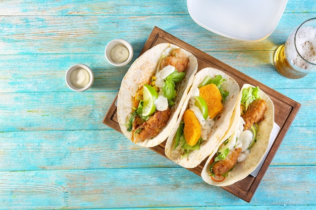 Deliciosos tacos de pescado en tablero de madera sobre fondo azul.