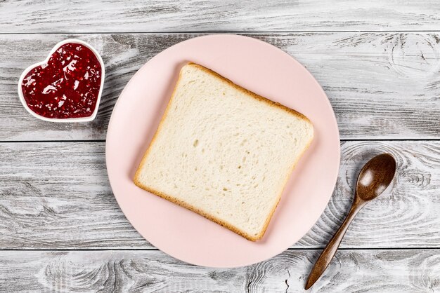 Deliciosos tostadas en placa rosa con mermeladas dulces y cuchara arbolada en mesa de madera.