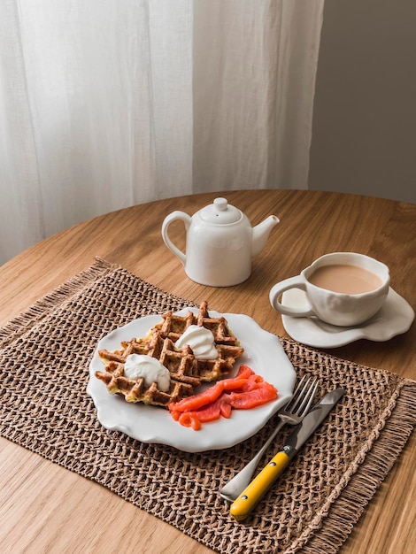 Foto deliciosos waffles de batata com creme azedo e salmão ligeiramente salgado e chá com leite em uma mesa de madeira