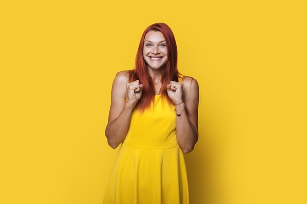 Delighed mujer de pelo rojo golpeando su puño en el aire aislado sobre fondo amarillo