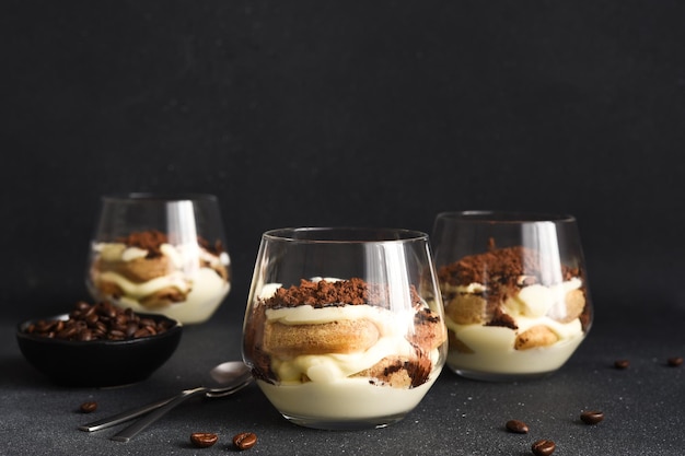 Delikates italienisches Dessert Tiramisu mit Kaffee in einem Glas auf schwarzem Hintergrund